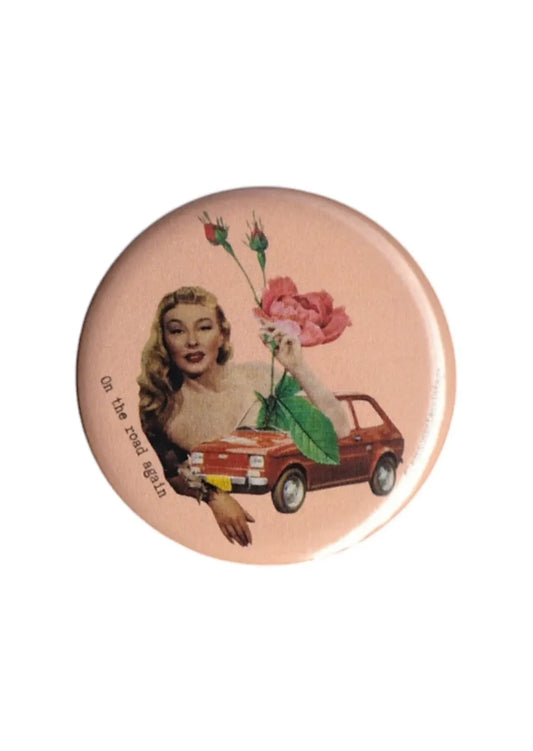 Badge vintage On the road again avec femme rétro, voiture ancienne rouge et fleur rose sur fond rose